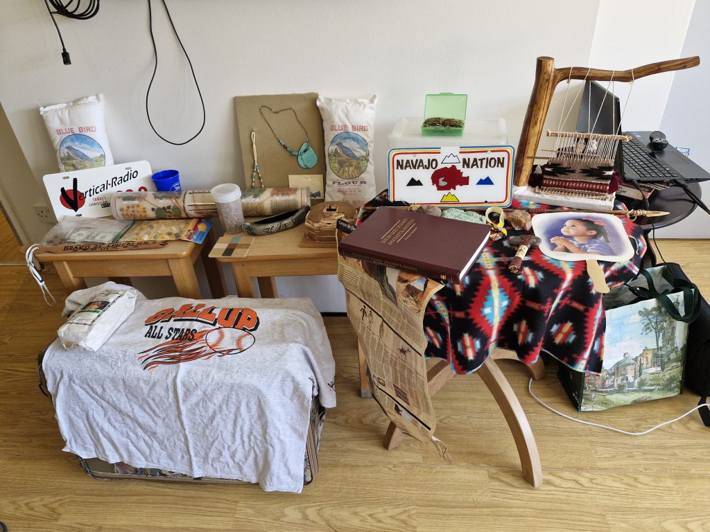 A wooden table displaying various items, including cultural artefacts, books, and textiles, set in a warm, inviting space.