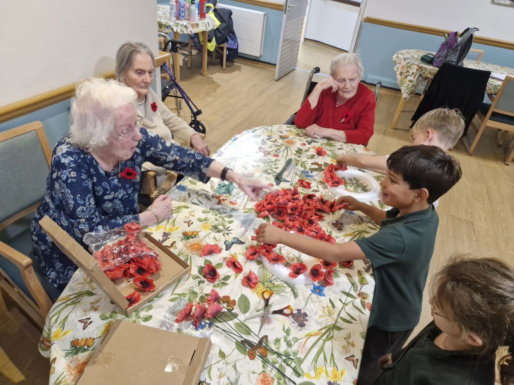 Residents and children engaging in an arts and crafts session, with poppy petals scattered on a table, creating a lively, communal atmosphere.