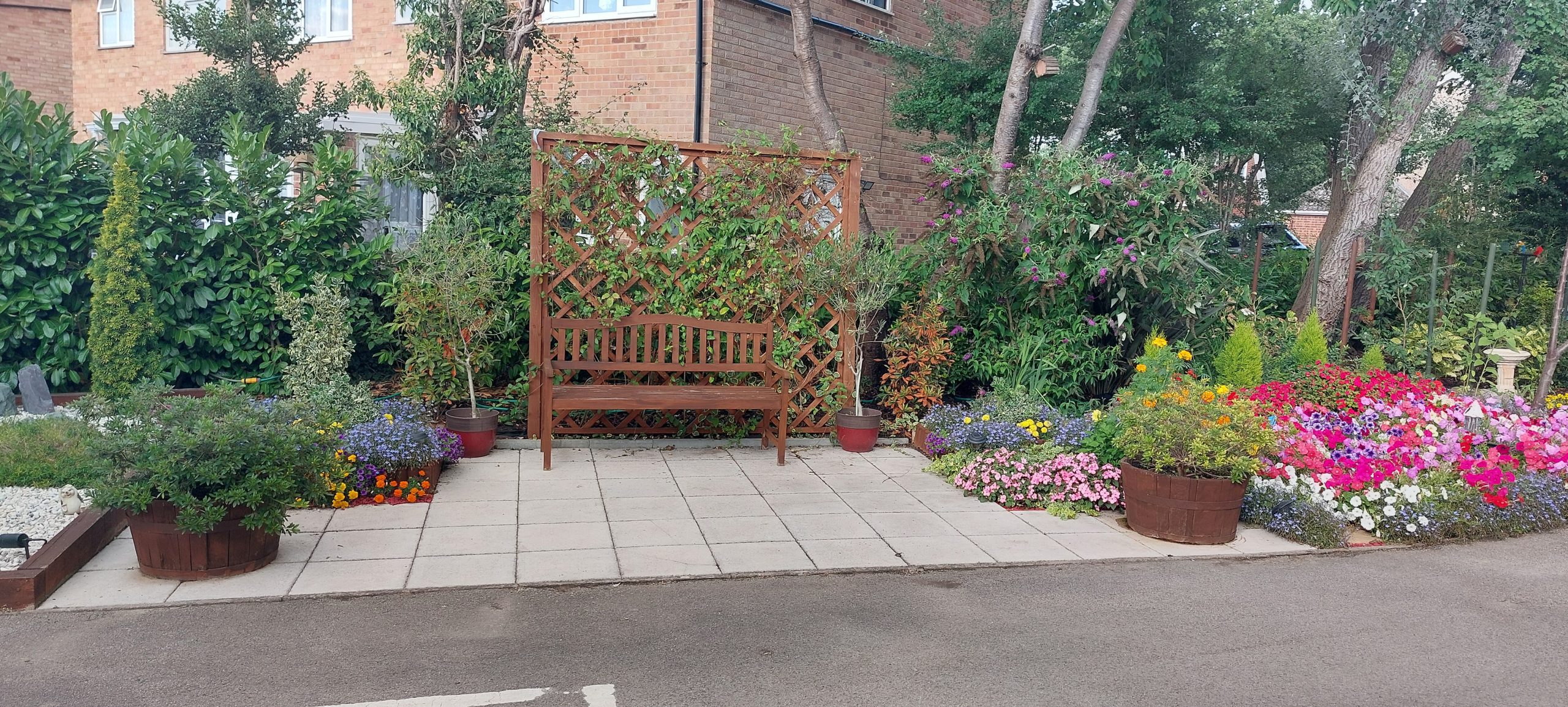 A peaceful garden area featuring a wooden bench surrounded by vibrant flowers in colourful pots and lush greenery.