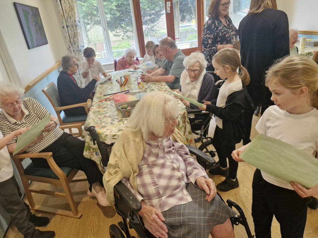 Residents and children engage in an activity around a table, with cheerful colours and a warm, homely atmosphere.