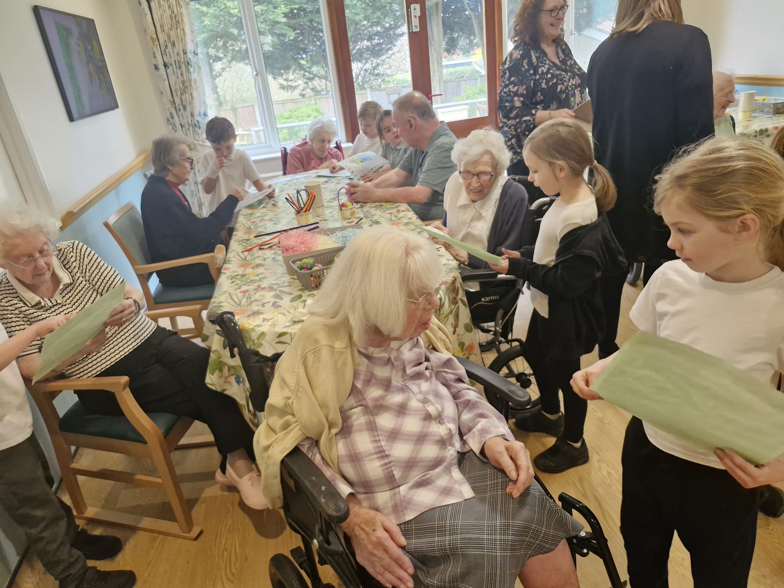 Residents and children engage in an activity around a table, with cheerful colours and a warm, homely atmosphere.